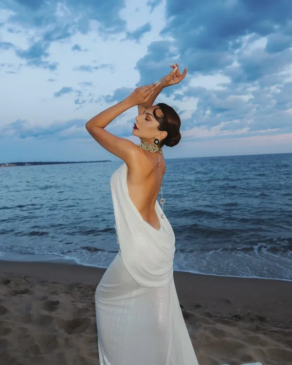 Pose dynamique bras levés sur plage de Cannes, robe pailletée argentée et maquillage glamour Sublimia