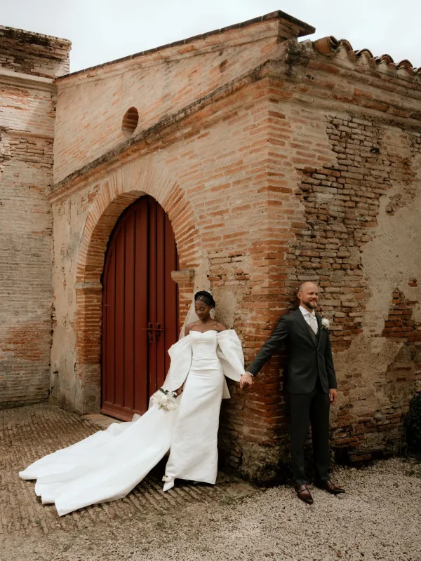 Couple de mariés devant arche en briques rouges, maquillage et coiffure naturel Toulouse Sublimia